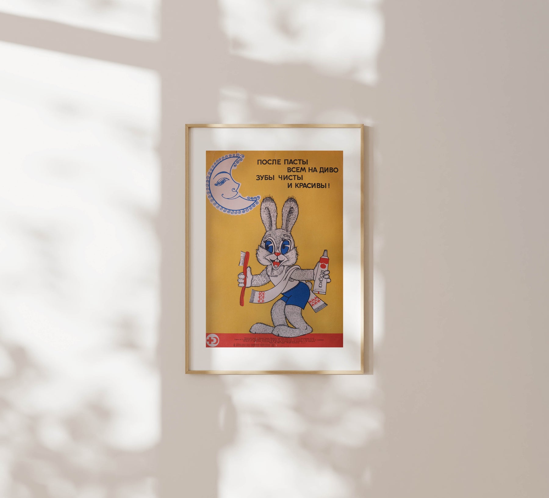 After Washing, Everyone's Teeth are Clean and Beautiful – Soviet Russia, hygiene awareness poster from 1982 by N, P, Petrova, featuring a rabbit holding a toothbrush a yellow background, framed in a wooden frame on a white wall with soft sunlight