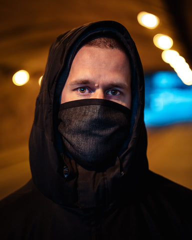 Homem vestindo jaqueta corta-vento, capuz na cabeça e máscara cinza escuro cobrindo a boca e o nariz