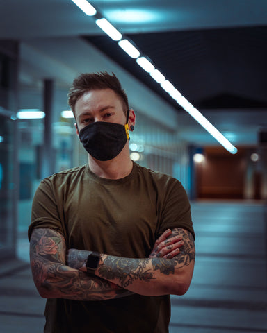 Joven con tatuajes que gastan una máscara negra con flores cruzando sus armas delante de su cuerpo