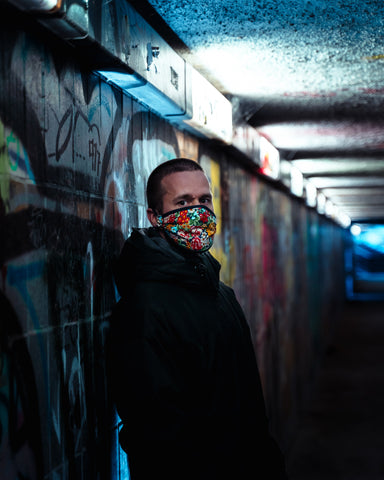 homem usando máscara facial de power flower encostado em uma parede coberta de grafite 