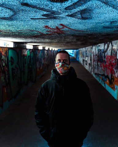Uomo che indossa la maschera per il viso fiore di potenza in piedi in un tunnel coperto di graffiti