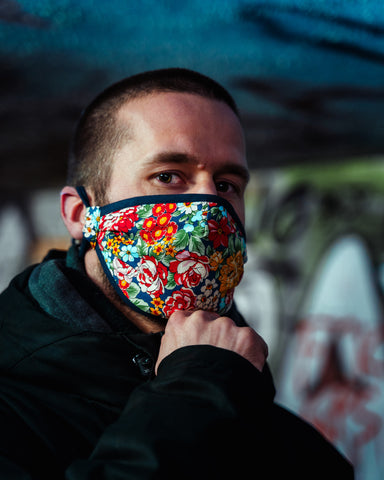 Joven vistiendo una colorida mascarilla de flores de poder con la mano en la barbilla 