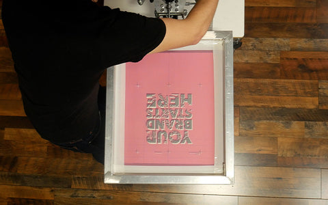 a person levels the print head on a Riley Hopkins press with a screen in the clamps