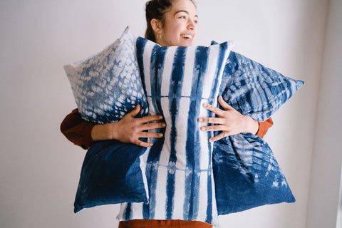 smiling woman holding 3 large indigo dyed cushions