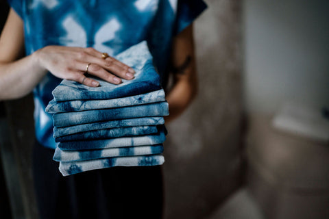 a woman in an indigo top holding a stack of indigo dyed tea towels