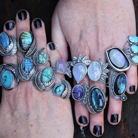 Stacks of silver rings across two hands. Made with silver, moonstone and opal