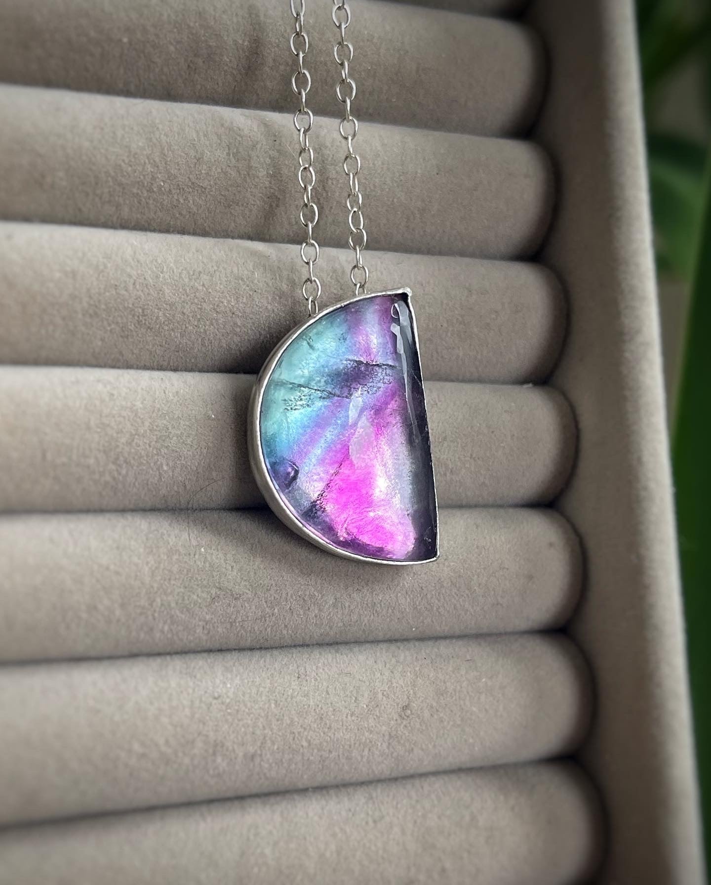 Purple, blue and pink fluorite necklace in sterling silver hanging on a background of a jewellery tray