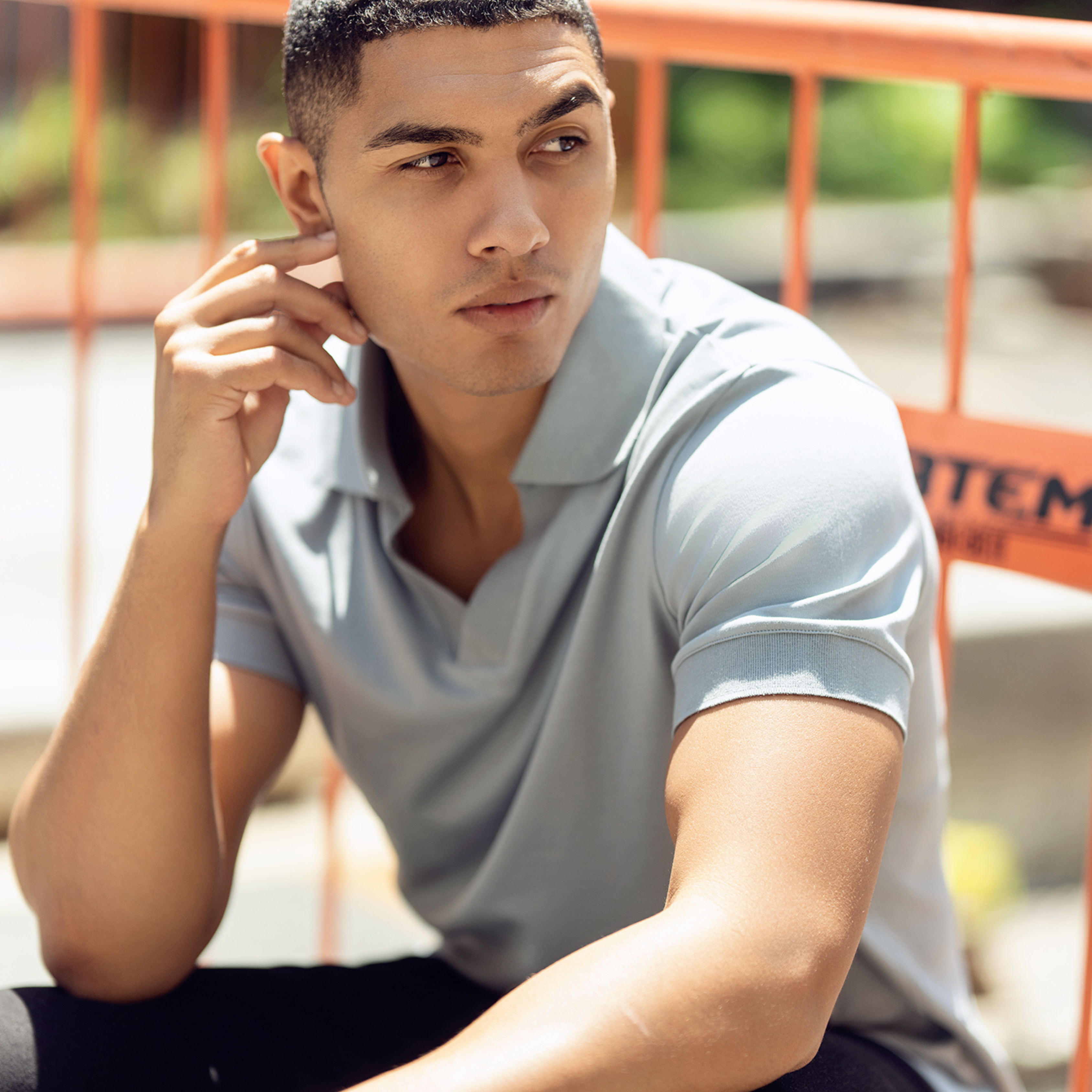 Young man in contemplation, seated by an orange barrier fence.