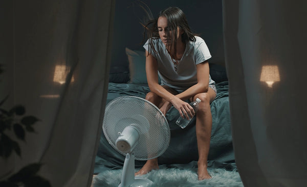 Frau sitzt auf Bett, schwitzt, zu heißes Schlafzimmer