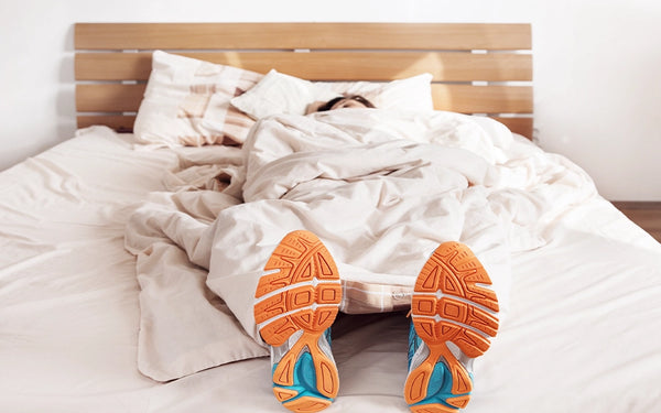 Einschlaftipp: von der Bewegung zu besserem Schlaf. Mann liegt mit Sportschuhen im Bett