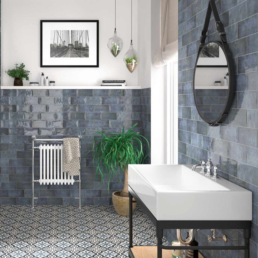 Jenson Azul Brick tiles 10x20cm and decorative tiles in a Victorian bathroom setting. Blue wall tiles cover the bottom half of the walls; the top half is painted white with shelving featuring a plant and bathroom products. Encaustic tiles as Victorian floor tiles, black metal, industrial style vanity units with rectangular white sink below round black metal mirror. Vintage style chrome radiator.