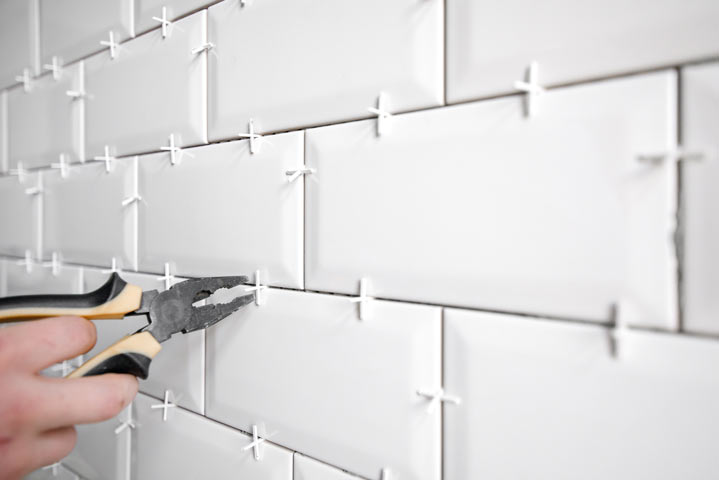 metro white tile with spacers sticking out of grout joints and pulled out of wall with pliers