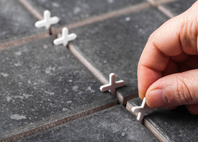 hand putting spacers into grout joints of grey tiles