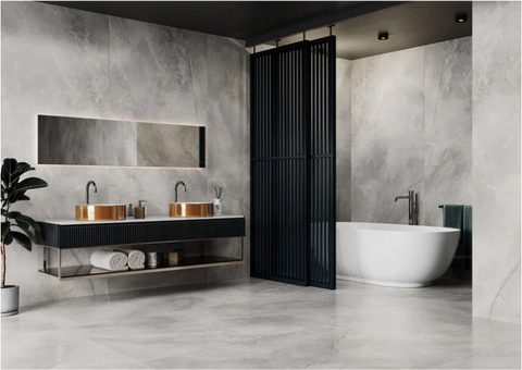 Wonderlust Silver large tiles 60x120cm in a bathroom setting. Tiled wall and floor with white bath, black partitions and paired bronze sinks in black unit.