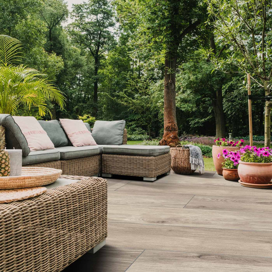 Outdoor Porcelain tile 30x120cm Arbour Natural Wood Paving in a garden setting with garden sofa and rattan table. trees in the background