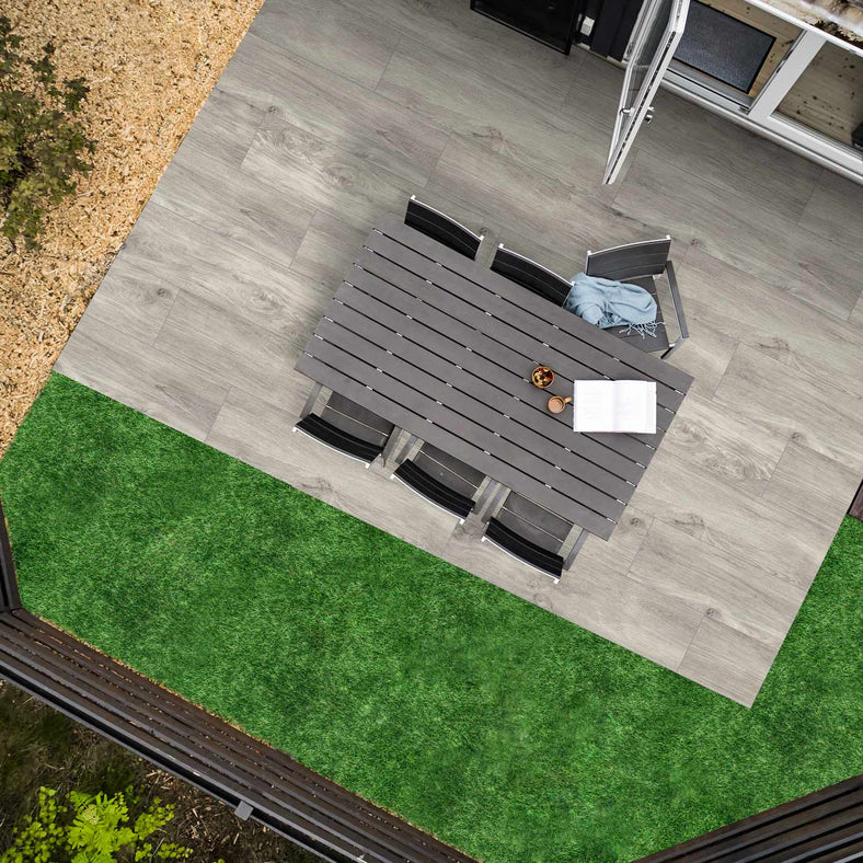 Outdoor Porcelain tile 30x120cm Arbour Bianco Wood Paving in a garden setting from an aerial position. wooden dining set with open book. open patio door and decking surrounded by grass and wood chippings