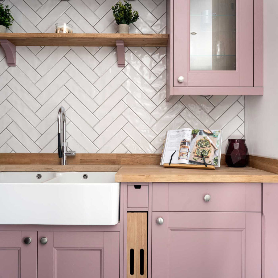 Cafe White Brick Tiles 7.5x30cm in a herringbone tile pattern as kitchen backsplash tiles. Pink kitchen cabinets with a belfast sink and shelving above.