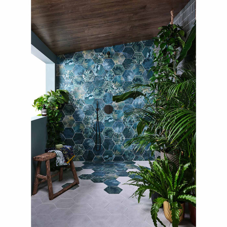 Jungle Hexagon tile 21.5x24.5cm in a wetroom setting. Tiles are on the shower wall and spill onto the floor. Features lots of green potted plants, a wooden stool and towels.