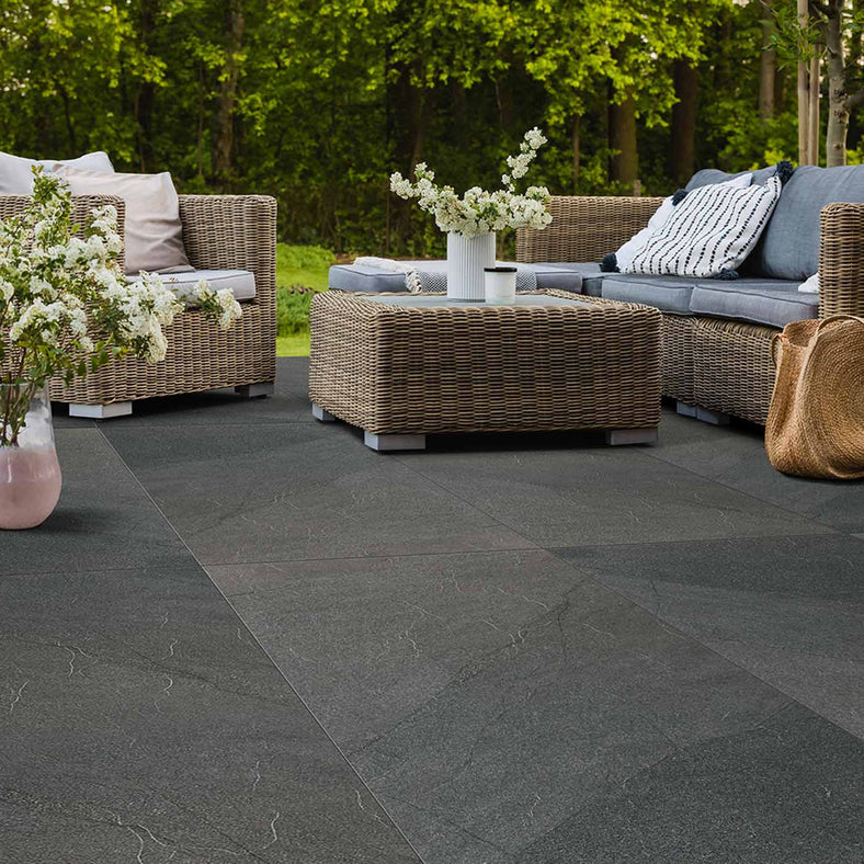 Outdoor Porcelain tile 60x120cm Hailes Anthracite in a garden seating setting with rattan sofa and coffee table next to a vase of flowers