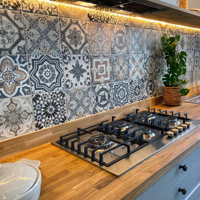 Nikea Matt mix patterned tiles set 20x20cm as kitchen splashback tiles. Close up of tiles in between navy kitchen cabinets. Wooden worktop with gas hob.