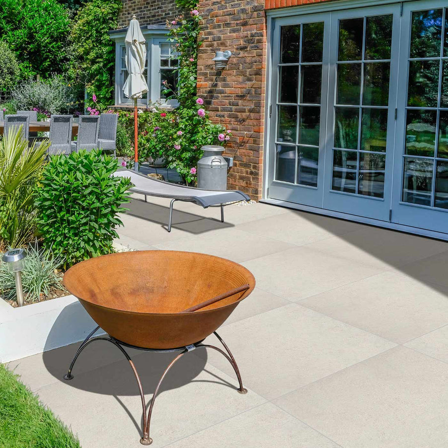 Lisbon Cream Outdoor Porcelain tiles 60x60cm in a garden setting with french patio doors, garden furniture and a rusty coloured firepit in the fore.