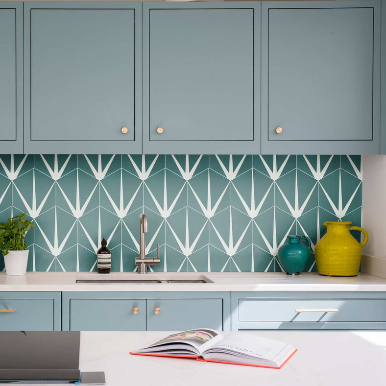 Ca' Pietra Lily Pad Eucalyptus Porcelain Tile 20x23cm. Hexagon tiles as kitchen splashback tiles nestled in turquoise kitchen units with white worktop, sunken sink and metal tap. Book placed on kitchen island.