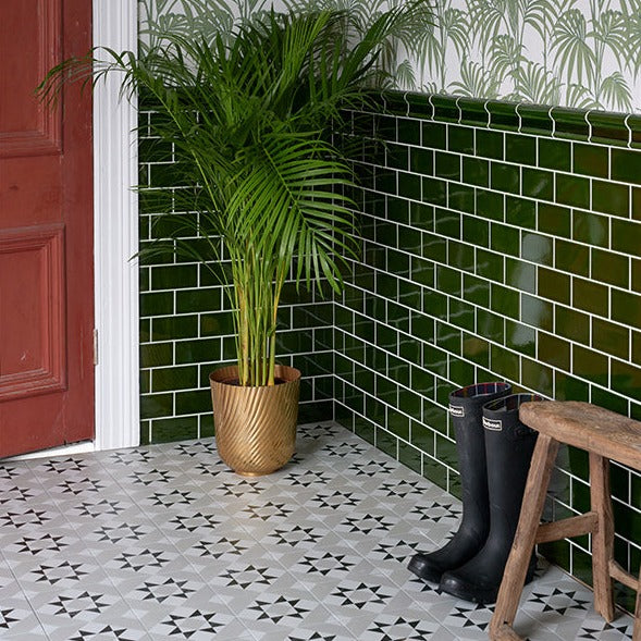 Brompton Borough Patterned tiles 20x20cm by Ca Pietra as hallway tiles. set ina period property with a red door, green metro tiles on the lower half of a wall and decorative green palm leaf tiles on the top half. A potted plant and black wellies are on the floor too.