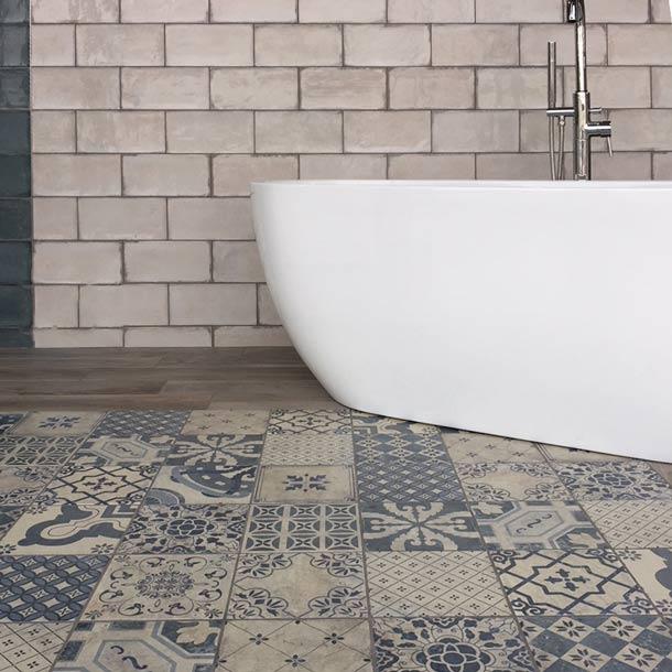 Antiqua mix patterned tiles set 20x20cm in a Victorian bathroom setting. Blue patterned Victorian floor tiles underneath a white, freestanding bath. Cream, vintage tiles to the wall.