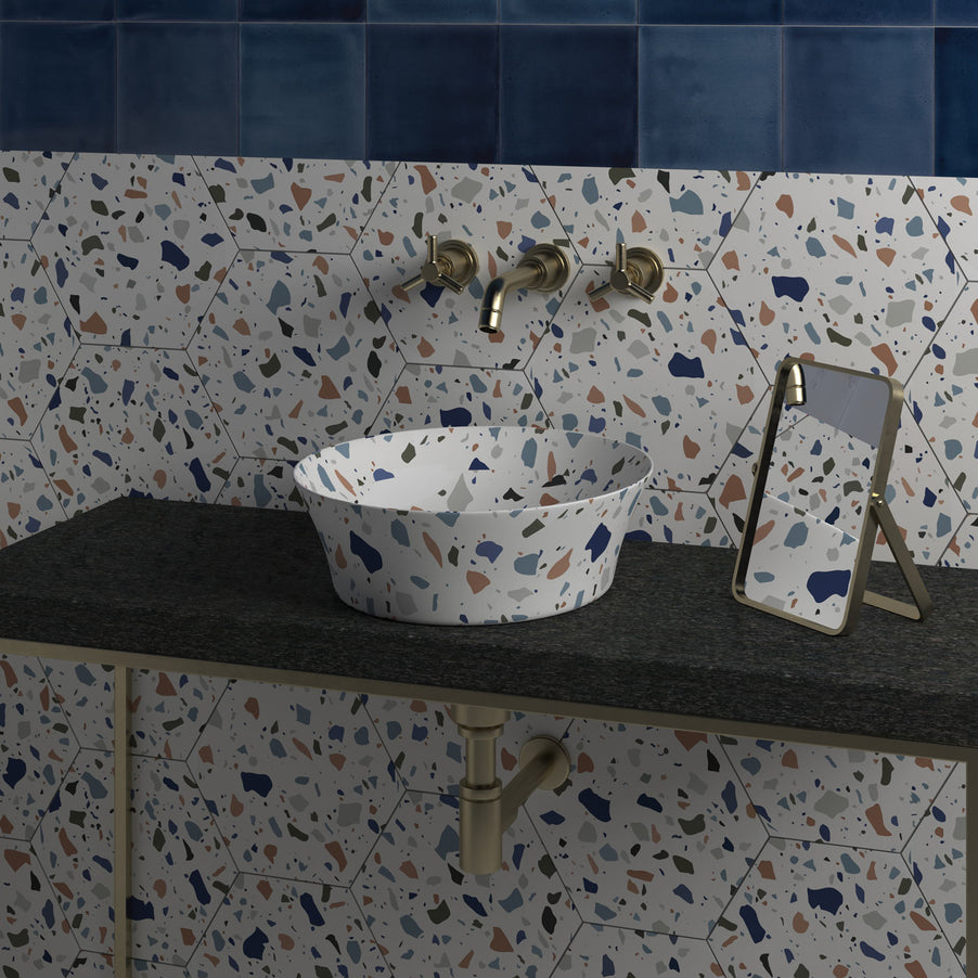 Terrazzo Hexagon tiles 21.5x25cm in a bathroom setting on the wall and vanity unit. Top half of wall is tiled in dark blue square tiles. Vanity unit has a sink in Terrazzo style, with gold taps coming out of the wall and small rectangular mirror to the side.