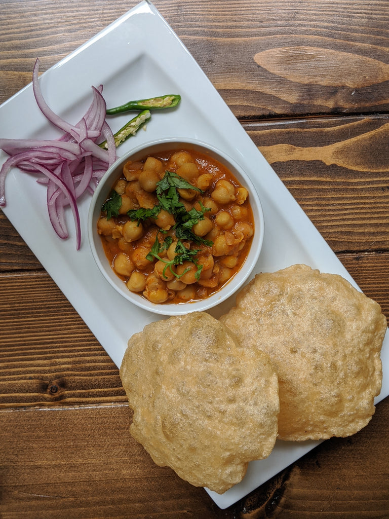 Showcasing a delicious bowl of Chole Masala made with SpiceFix chole masala blend and other aromatic spices. The dish is completed with onion relish and fluffed Indian bread (Poories) on the side