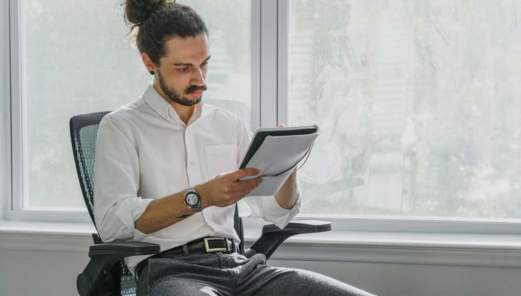 man in white shirt with leather belts on black pants in office chair