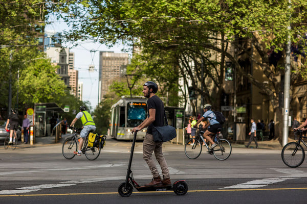Man riding an electric scooter through a city with a tram in the background