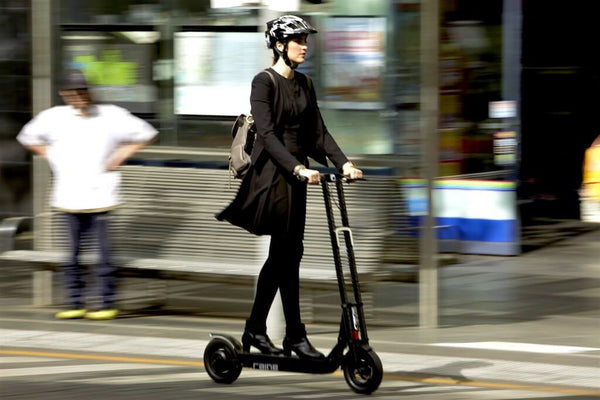 Woman riding electric scooter safely through city with a helmet