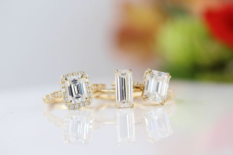 Three emerald-cut diamond engagement rings with flowers in the background