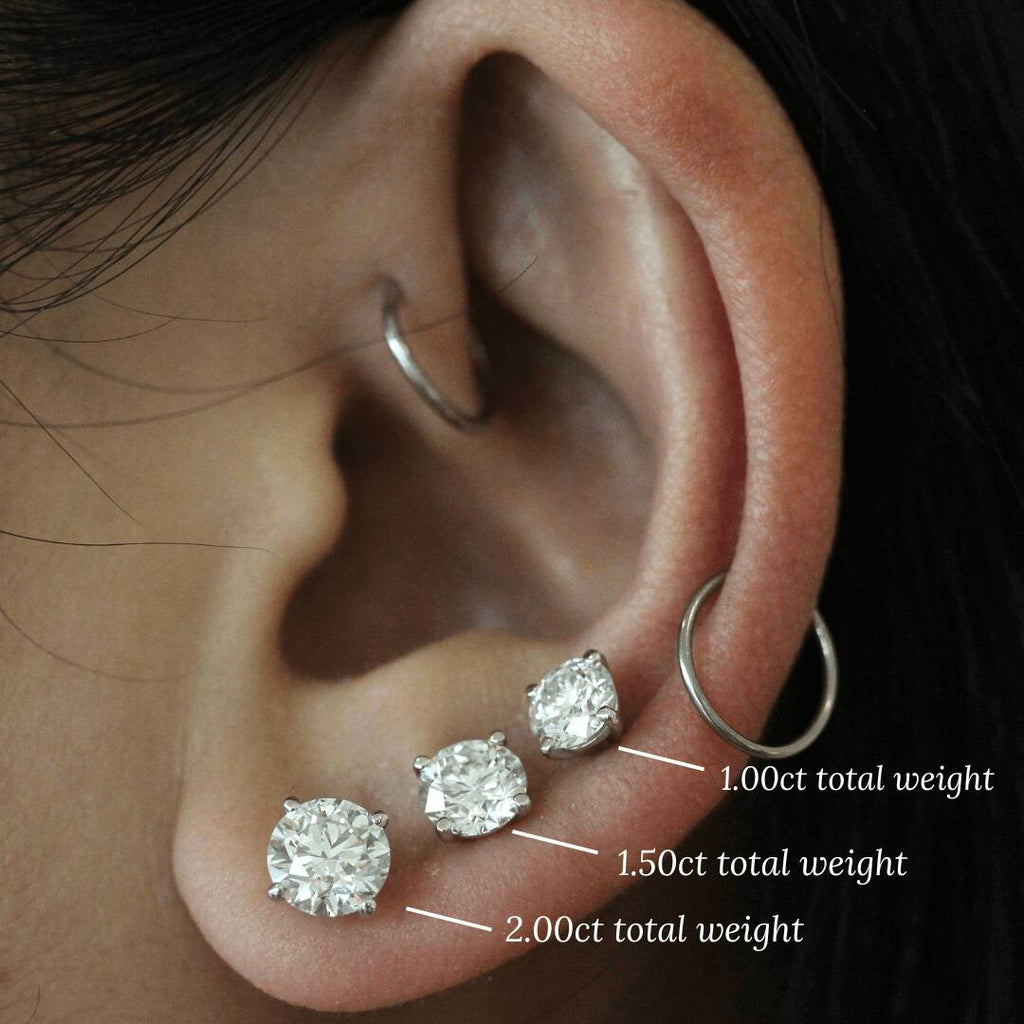 three sizes of diamond stud earrings modeled on an ear