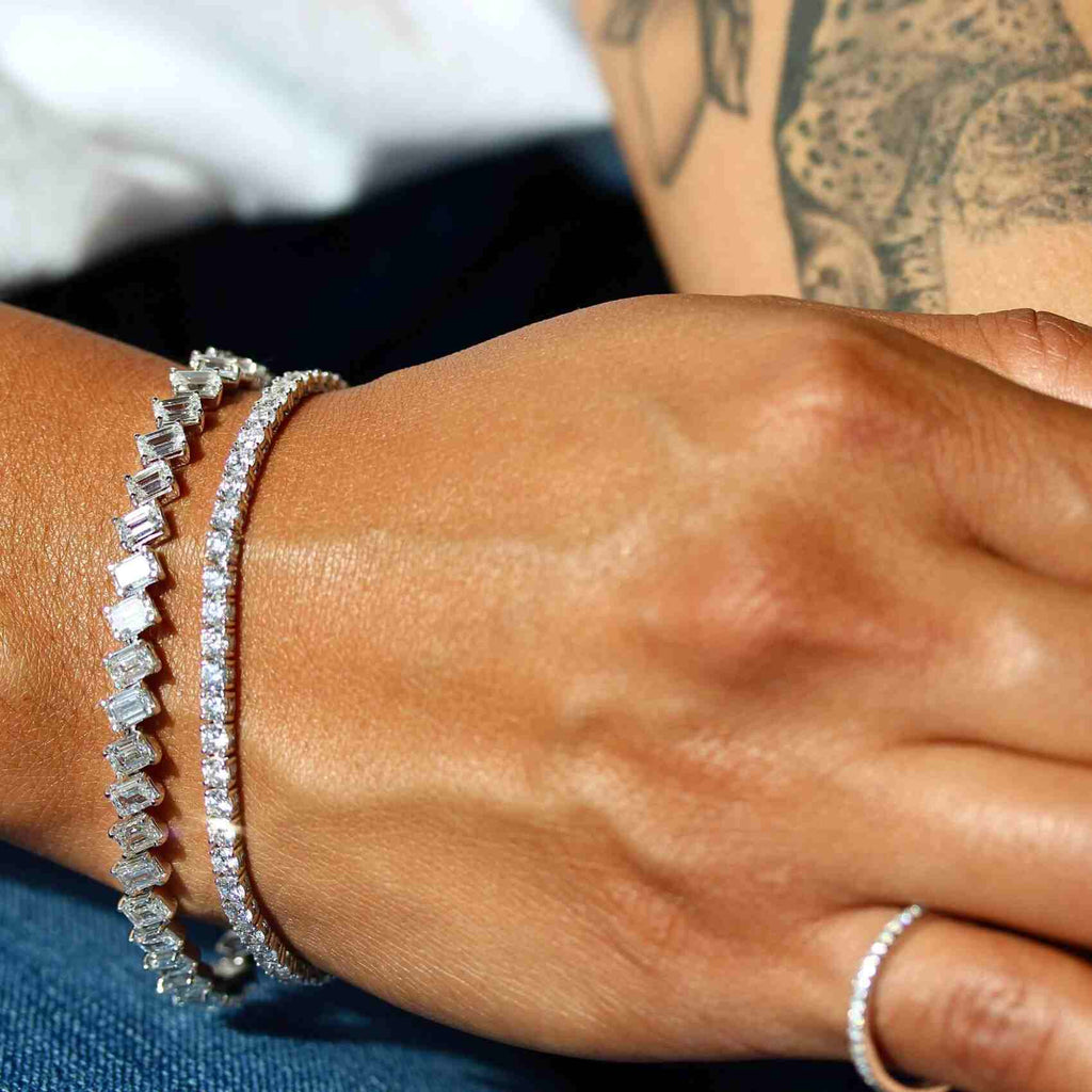 hand with two diamond tennis bracelets and a pinky ring
