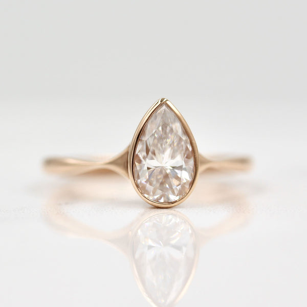 Pear-shaped Diamond with a Rose Gold Band on White Background and Surface