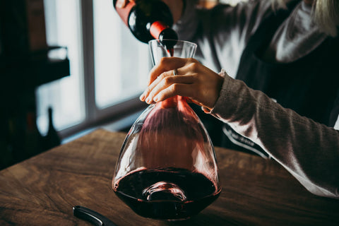person pouring red wine into a decanter