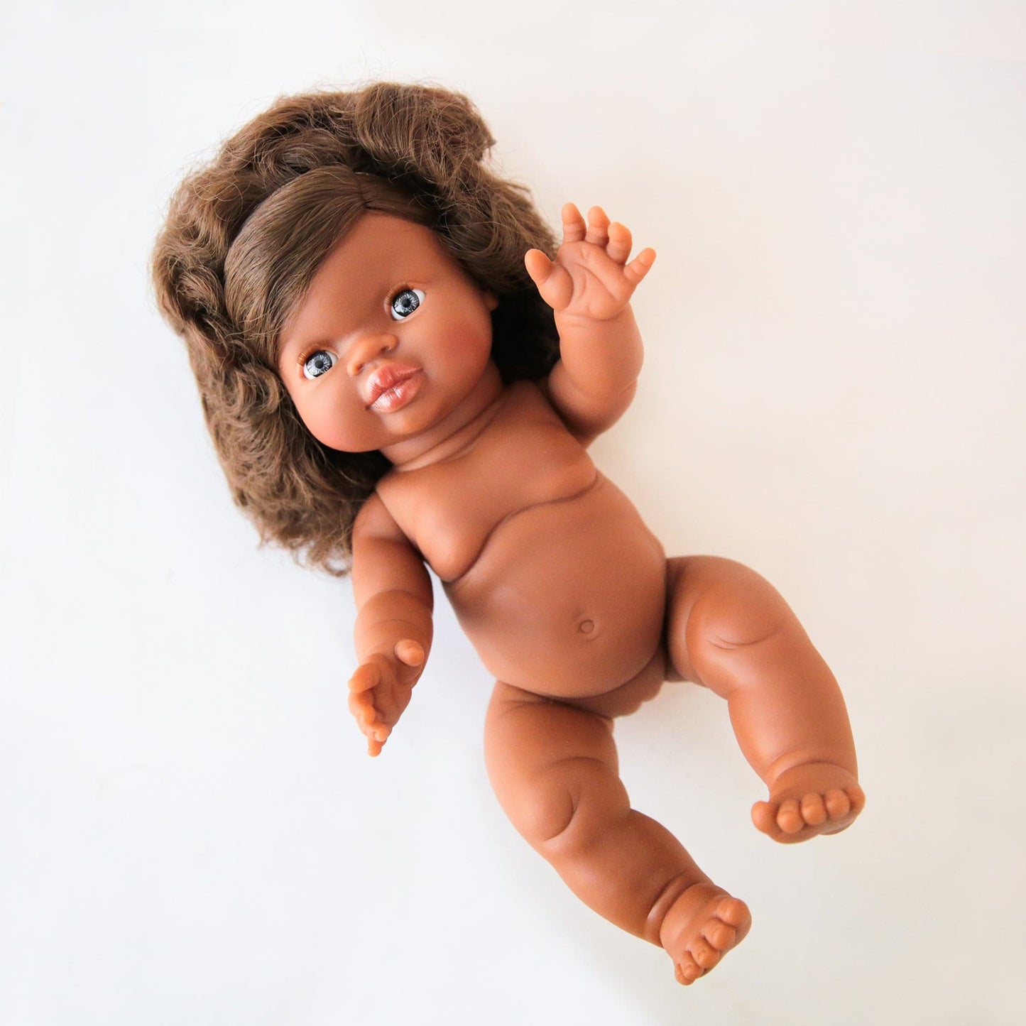 In front of a white background is a baby doll with dark brown curly hair.