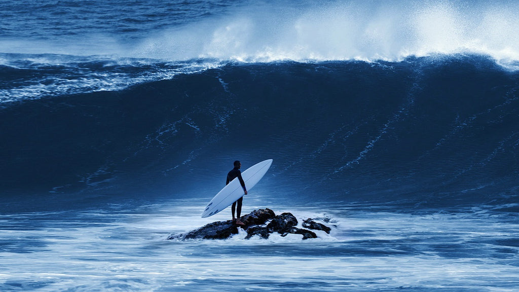 Garrett McNamara standing on water rock, gazing at colossal wave – surf adventurer in awe.