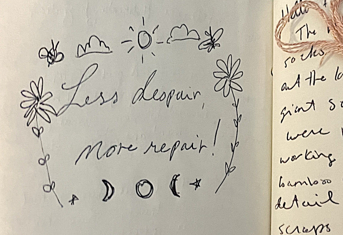 The words "Less despair, more repair" doodled in black pen on the Swift Darning Loom's guest book/passport. The phrase is surrounded by nature motifs (sun, moon, flowers, clouds, and bees)