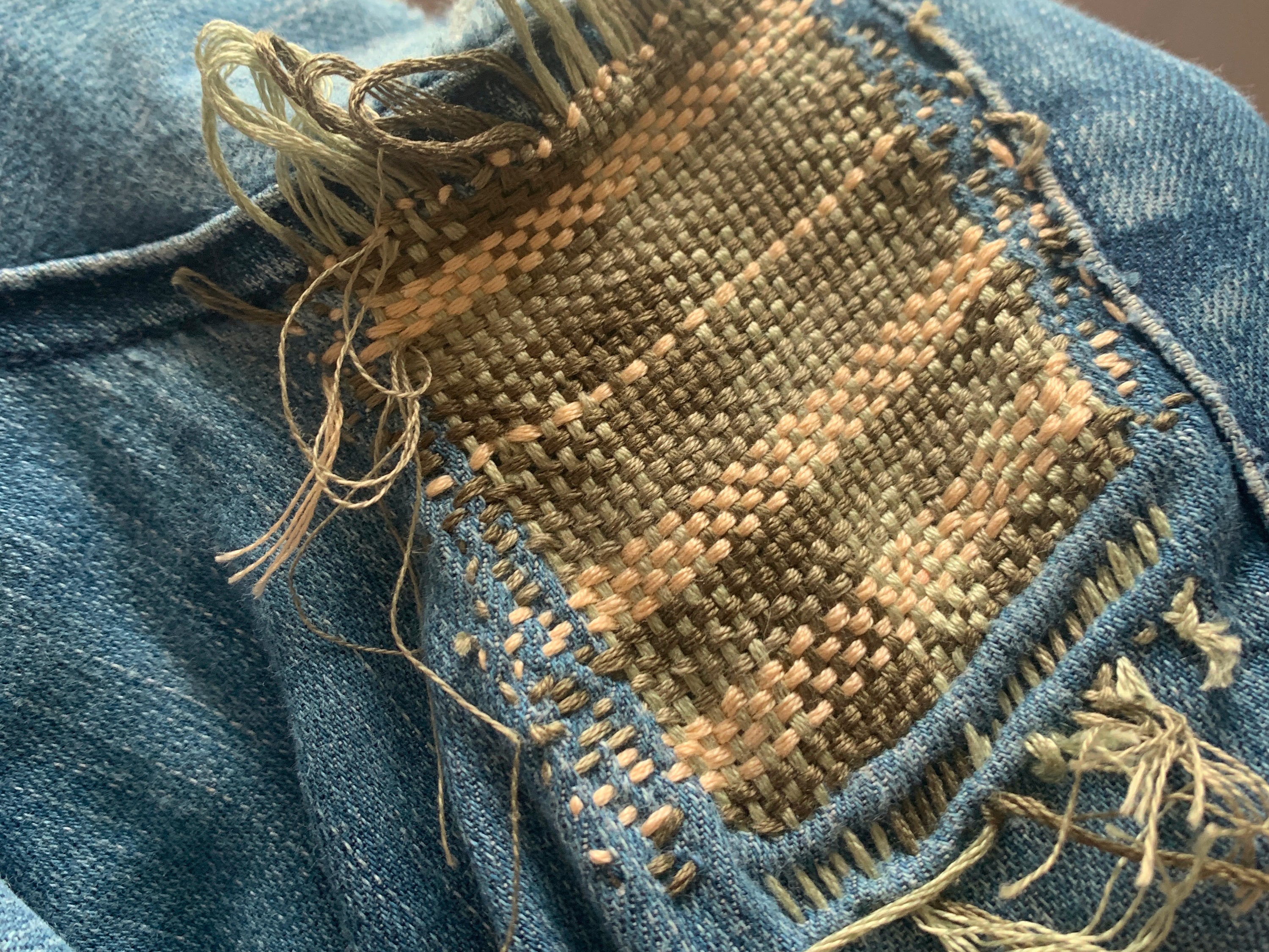 Close up of finished plaid patch on blue denim. Woven with multiple colours of embroidery floss, the ends still need to be secured but it's looking lovely.