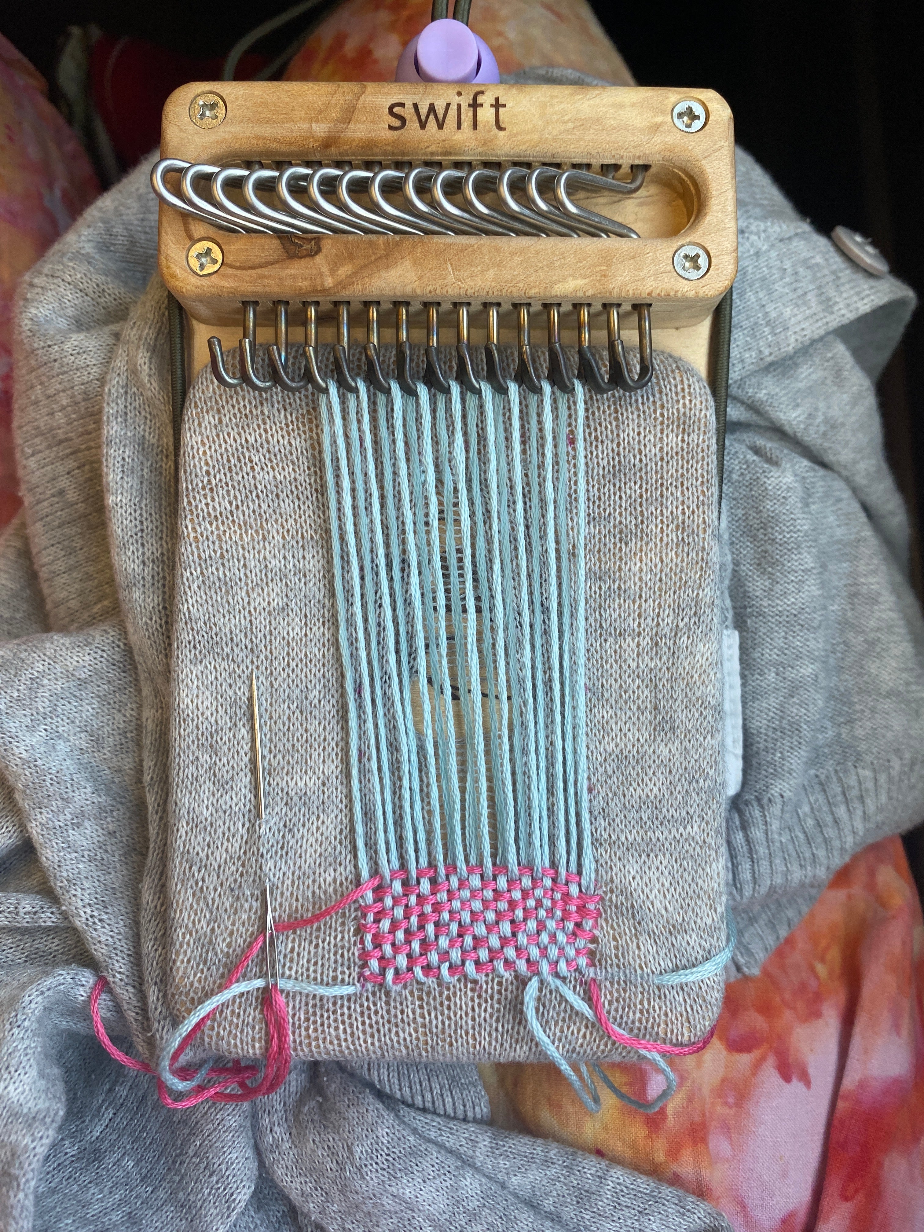 Swift Darning Loom in-progress visible mending with blue and grey thread on a grey sweater
