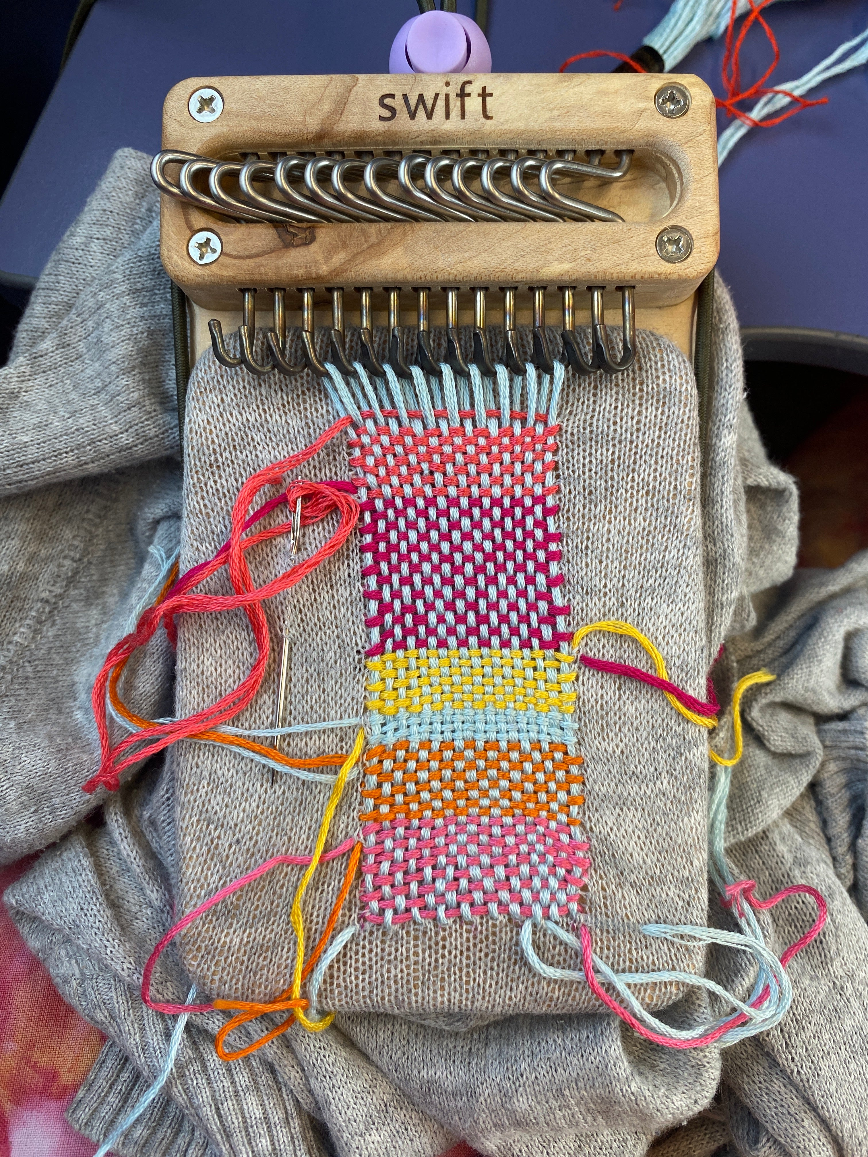 Swift Darning Loom visible mending in progress on a grey cardigan woven with some very bright shades of pink, orange, blue, yellow and green.