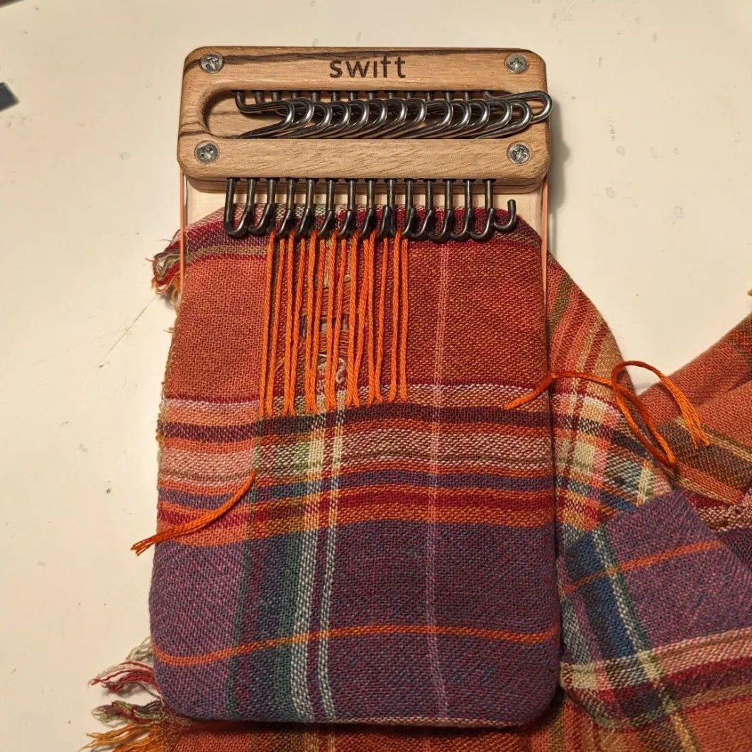 Swift Darning Loom set up with orange warp strands on a jewel-toned plaid napkin.