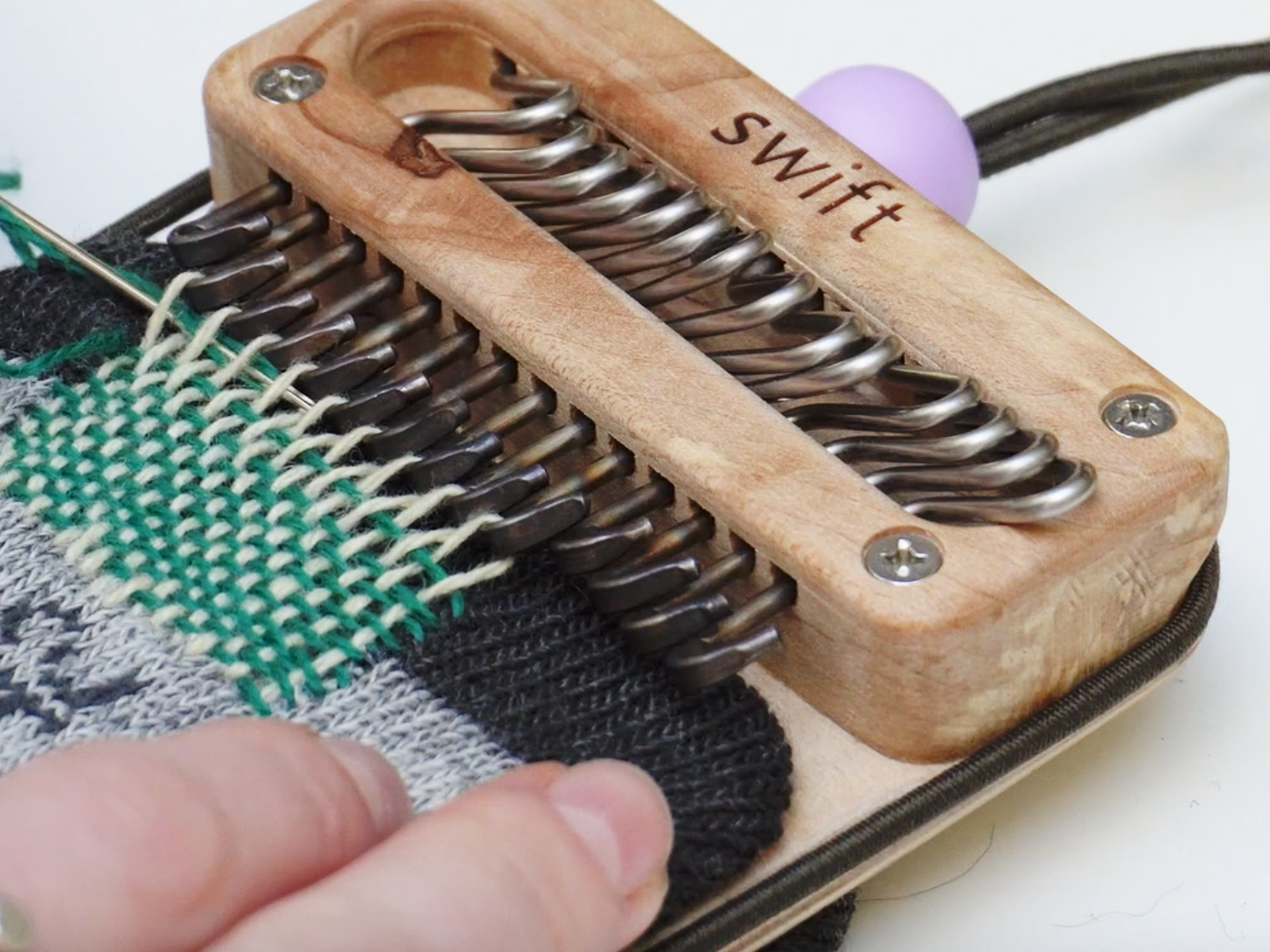 a close up of skye using the swift darning loom to repair a grey sock in shades of teal.