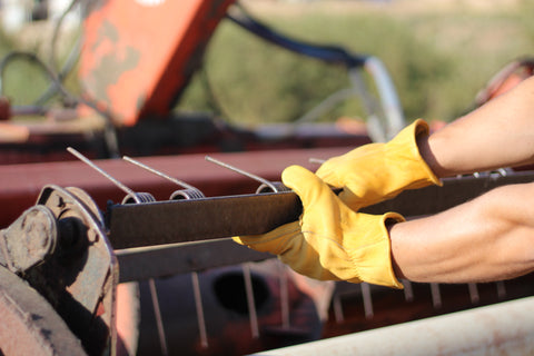 arms and hands shown wearing iron fencer leather work gloves fixing a tractor