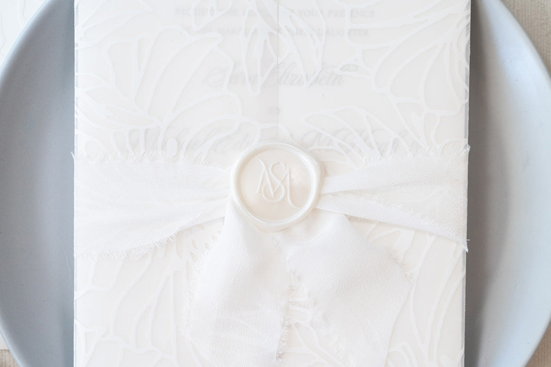 Vellum wrap with bold white florals in white on white, paired with delicate wide white silk ribbon and a custom monogram wax seal