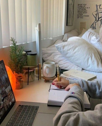 writing at a desk with laptop in front and bed behind