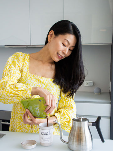 A young woman pouring bone broth from a pouch into a cup. 